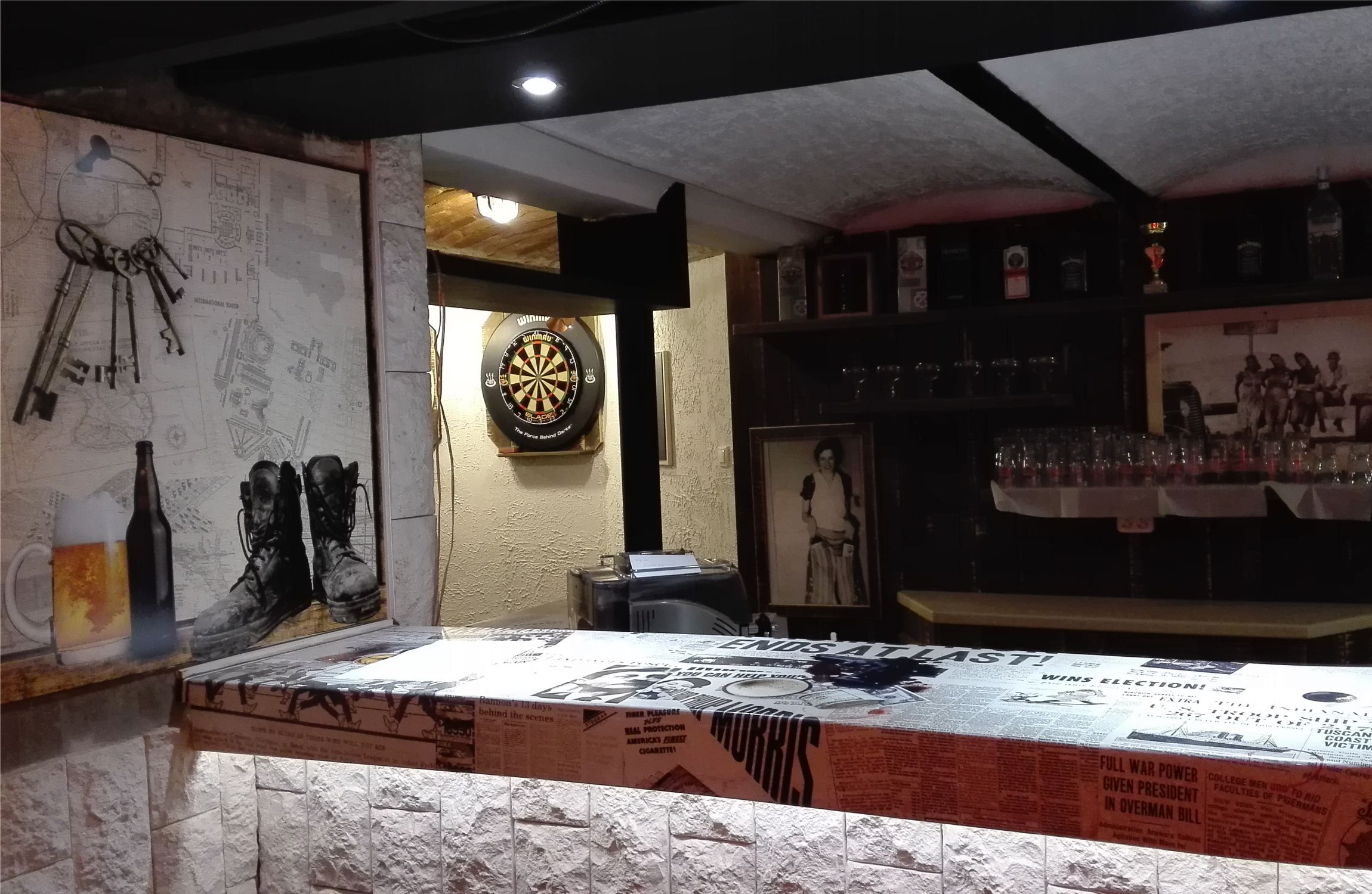 Régi újságpapír foszlányokkal dekorált söntéspult, háttérben dartstábla