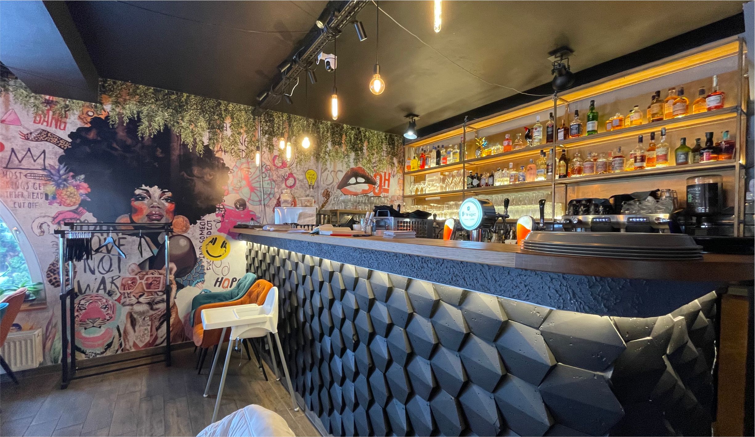 Étterem absztarakt és fekete burkolatú pultja, háttérben funky nőt ébrázoló egyedi tapétával és színes streetart formákkal